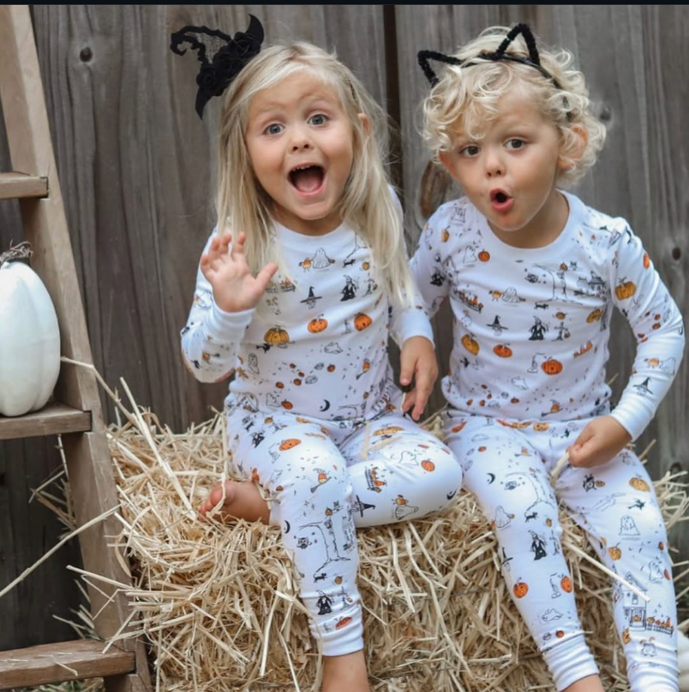 Two children wearing matching Petidoux Trick or Treat Town Halloween pajamas